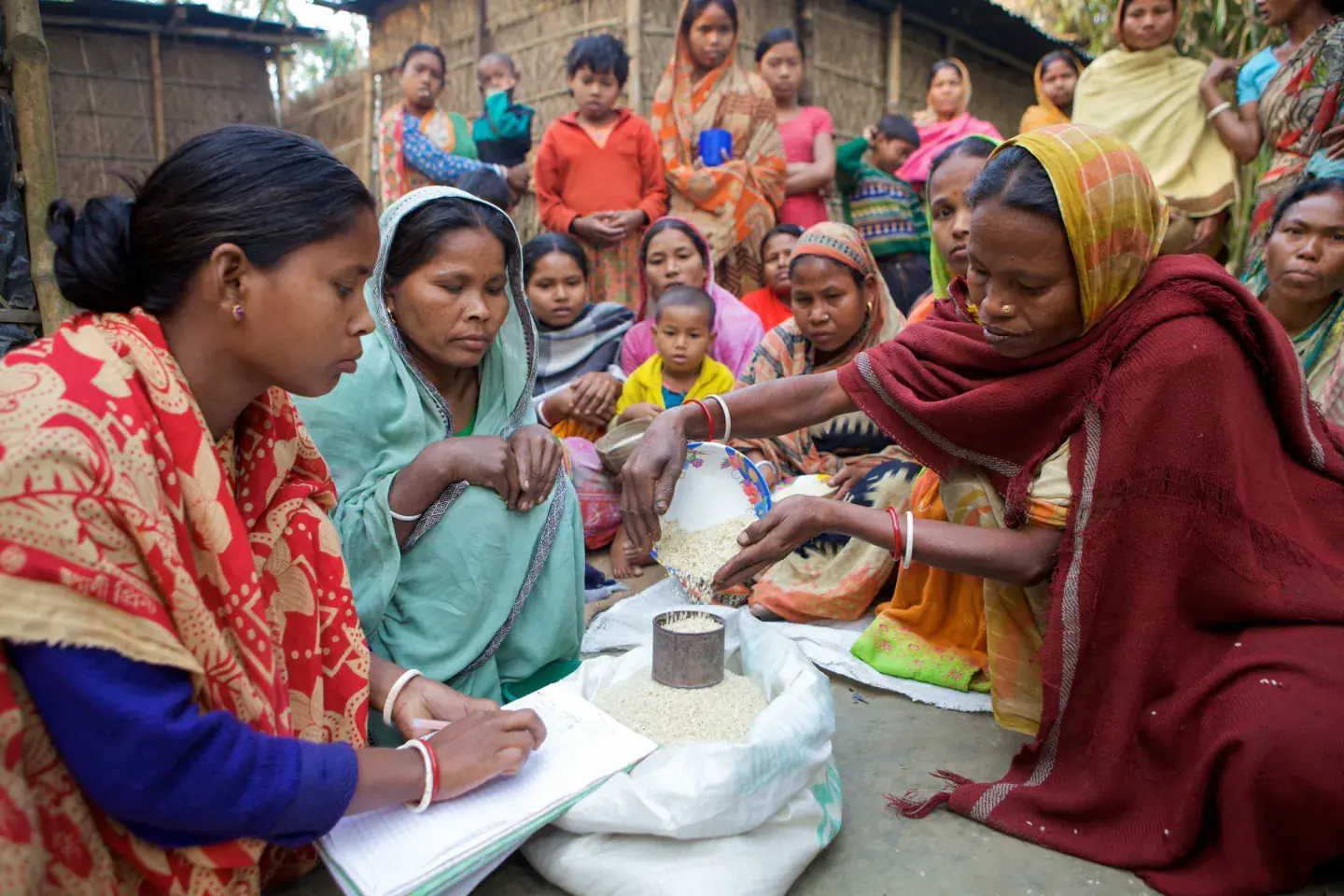 Women recording and measuring a shared grain store during a village development meeting